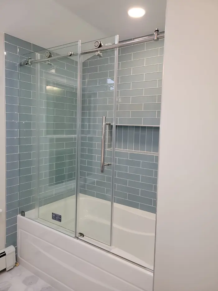 Bathtub with sliding glass doors and sea-glass blue subway tile surround with built-in niche