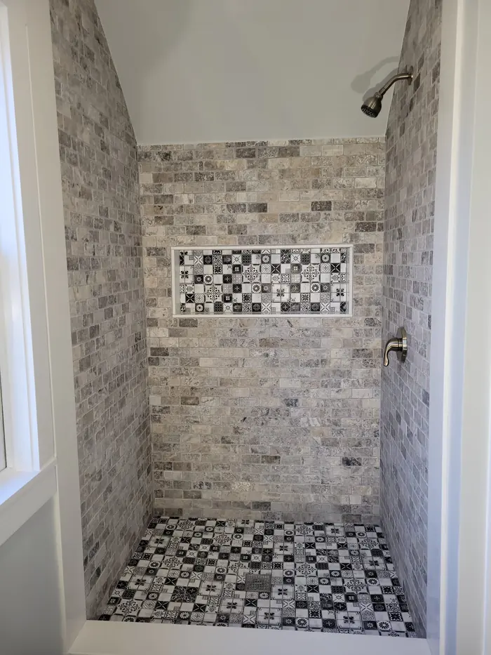 Walk-in shower with grey stone subway tile walls, a patterned mosaic niche and black and white mosaic floor